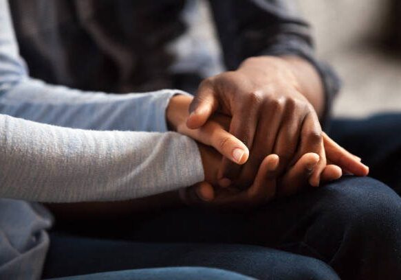 Close up black woman and man in love sitting on couch two people holding hands. Symbol sign sincere feelings, compassion, loved one, say sorry. Reliable person, trusted friend, true friendship concept